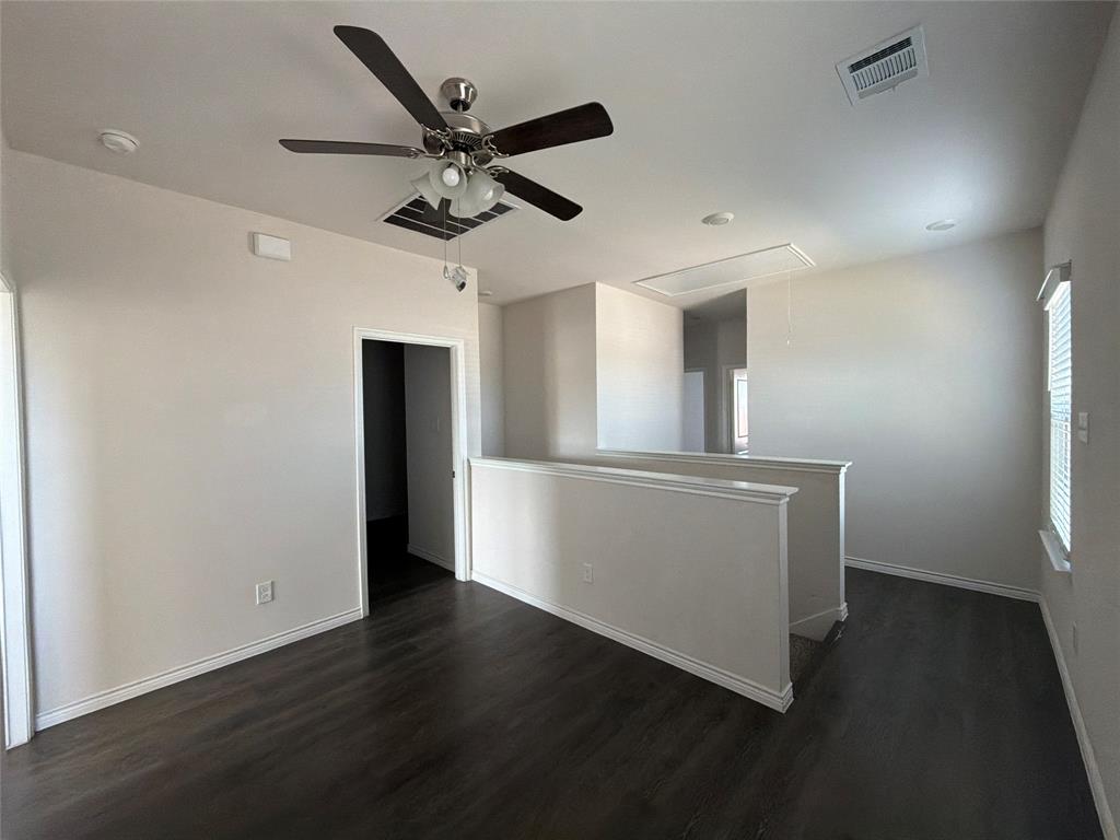 Open-concept space featuring dark wood-finish flooring, a multi-blade ceiling fan with integrated lighting, neutral wall paint, and natural illumination provided by a side window