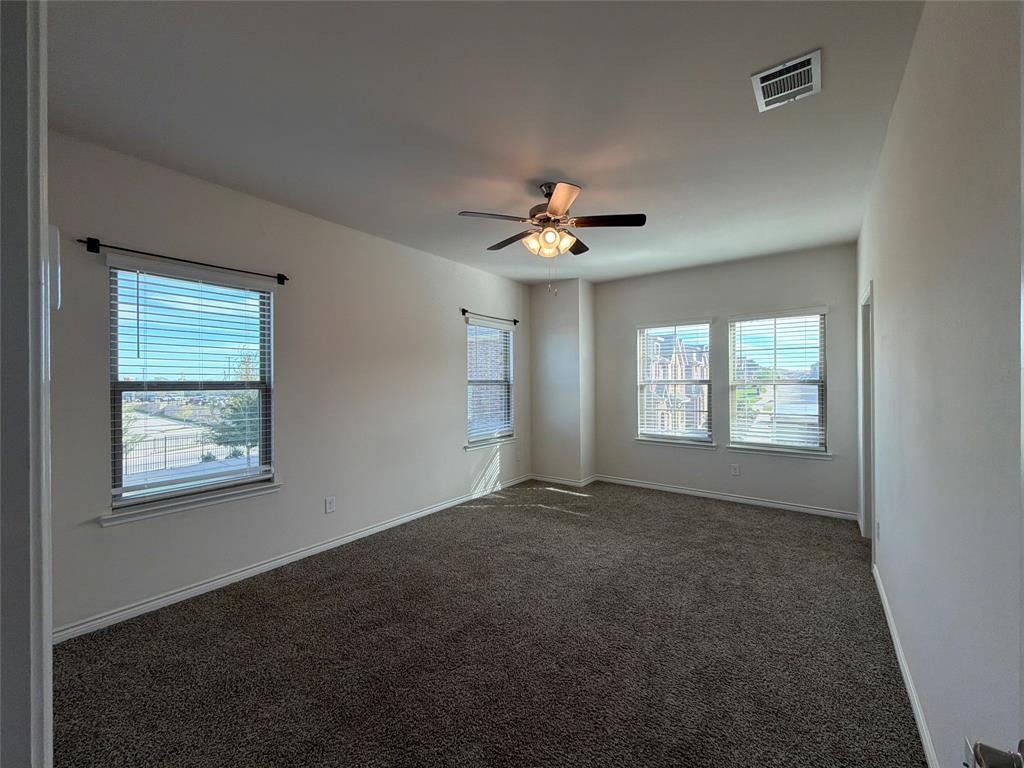 Neutral interior space featuring wall-to-wall carpeting, three windows with blinds, and a centrally mounted ceiling fan with integrated light fixture