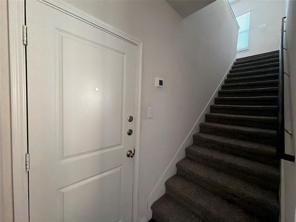 Entryway featuring a solid panel door with metallic hardware, neutral wall paint, and a carpeted staircase with a metal handrail