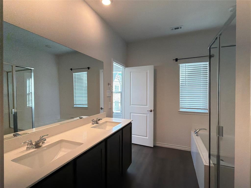 Dual vanity with solid-surface countertops, undermount sinks, full-width mirror, separate bathtub, and glass-enclosed shower