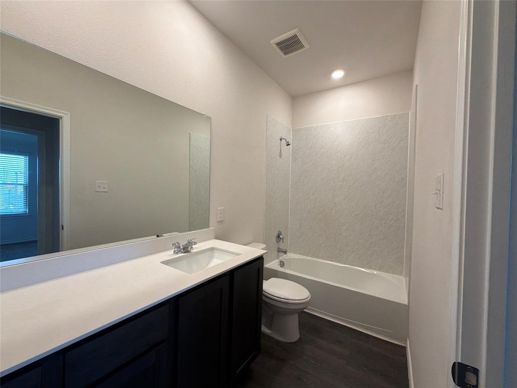 Bathroom featuring a white vanity with a rectangular undermount sink, a large wall-to-wall mirror, dark wood-finish cabinetry, and a tub-shower combination with textured wall surround