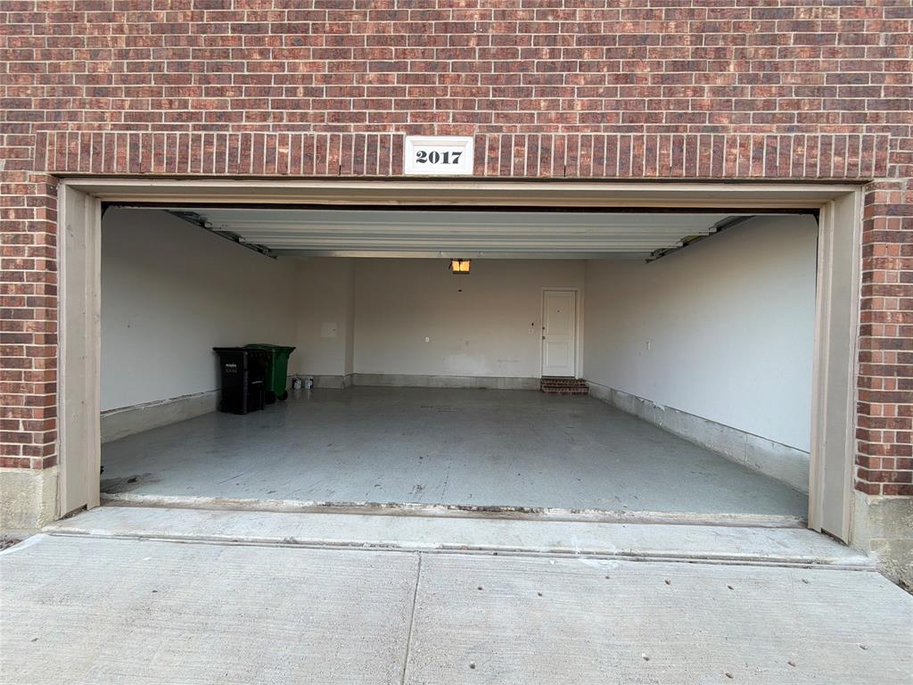 Attached garage featuring a brick exterior facade, concrete floor, overhead door, and interior door access