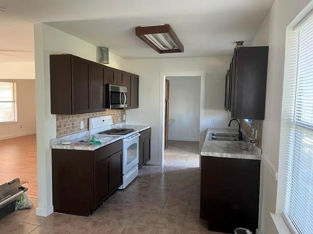 Kitchen featuring dark-finish cabinetry, stone-pattern countertops, a tiled backsplash, and stainless steel built-in microwave
