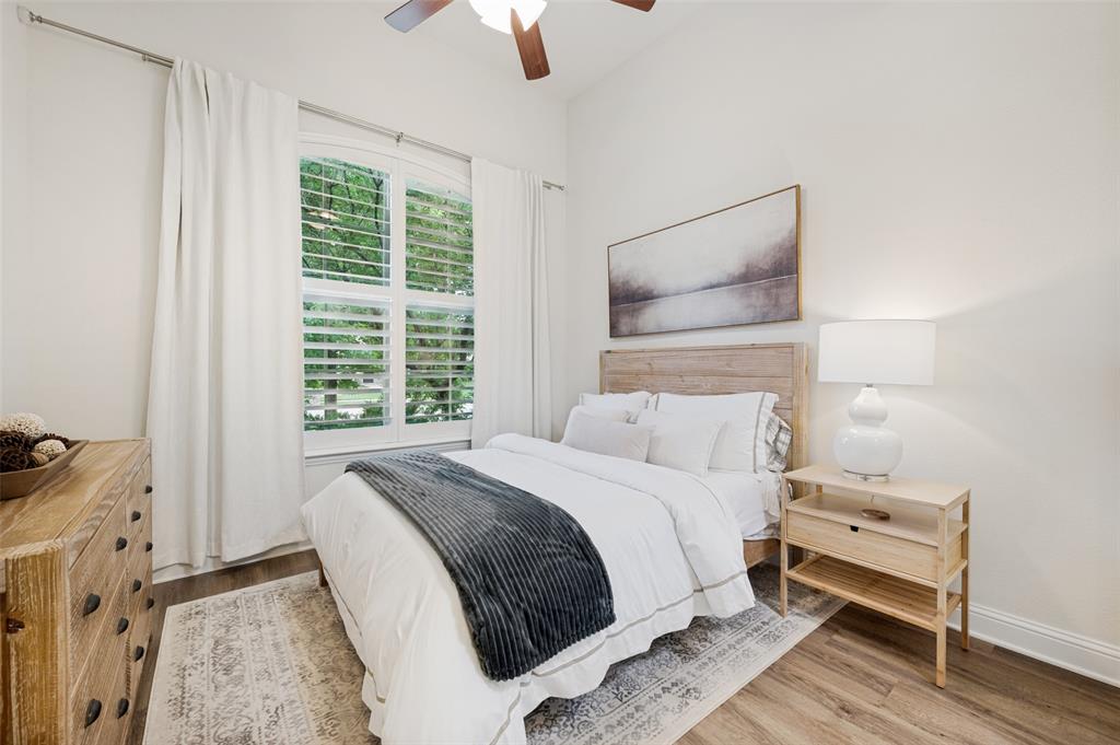 Downstairs guest room with ensuite bath - Vaulted ceiling with a ceiling fan, wood-finish flooring, plantation shutters, and an arched window
