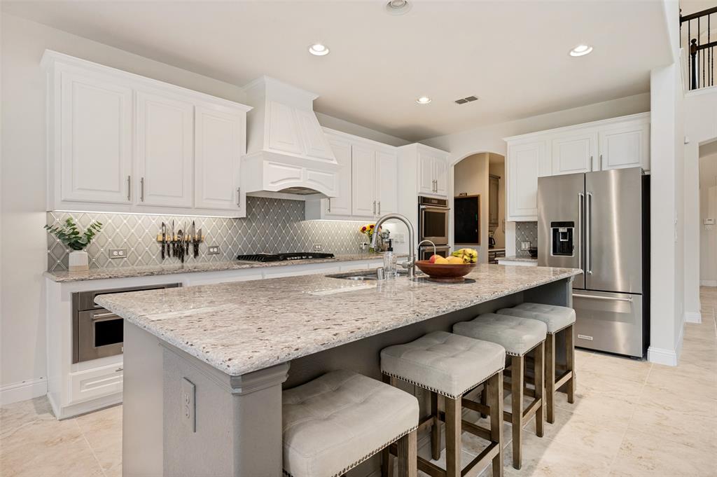 White cabinetry, stainless steel appliances, large kitchen island with light-toned countertop, recessed lighting, and tile flooring