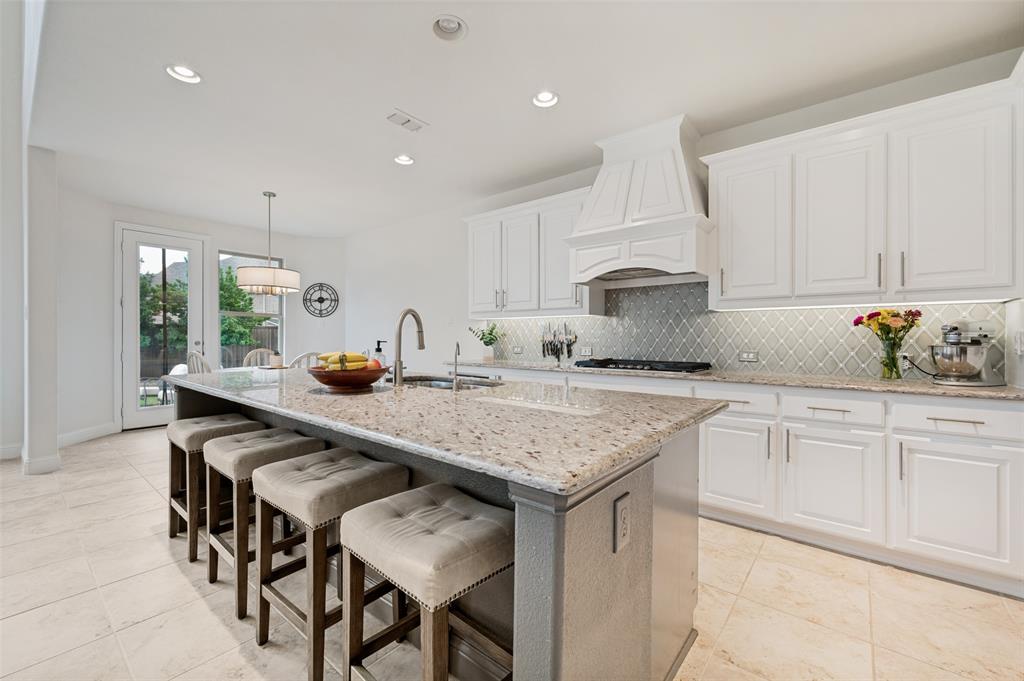 Kitchen featuring an expansive island with granite countertop, white cabinetry with under-cabinet lighting, a patterned tile backsplash, and tile flooring
