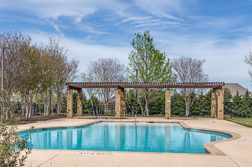 Curved swimming pool with concrete decking, stone-columned pergola, and surrounding mature trees