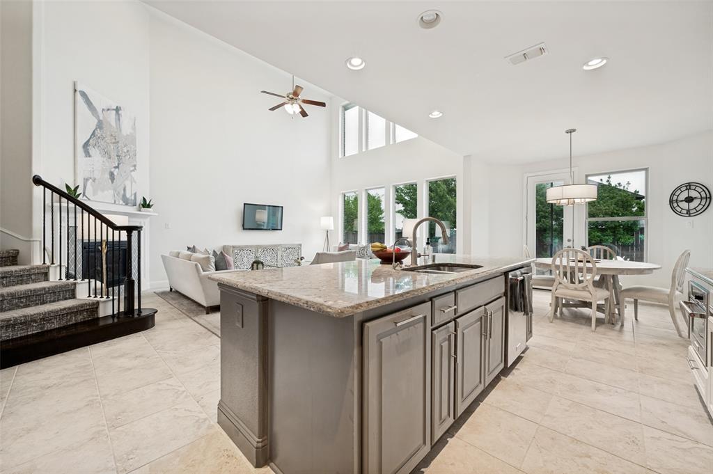 Open-concept living space featuring high ceilings, a kitchen island with stone countertop, tile flooring, and a fireplace with a mantel