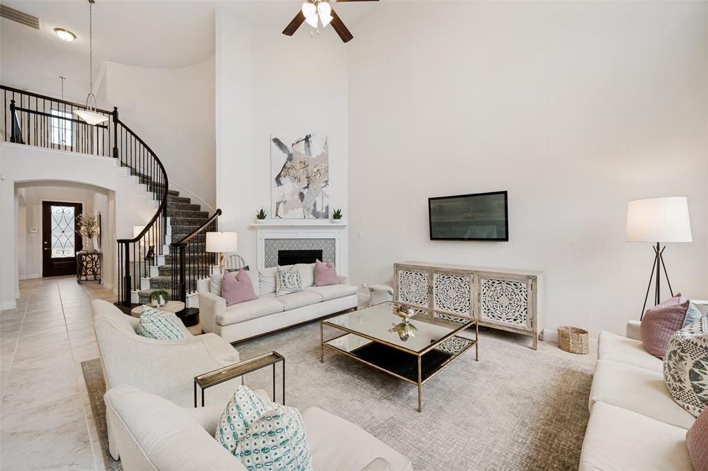 Two-story living area featuring a fireplace with decorative tile surround and mantel, curved staircase with metal spindles, and a ceiling fan