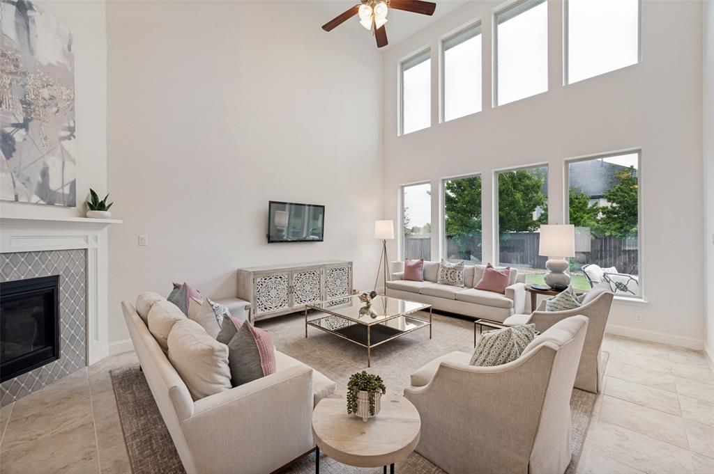 Two-story living area with high ceilings, fireplace with decorative tile surround, built-in media console, and a series of tall windows
