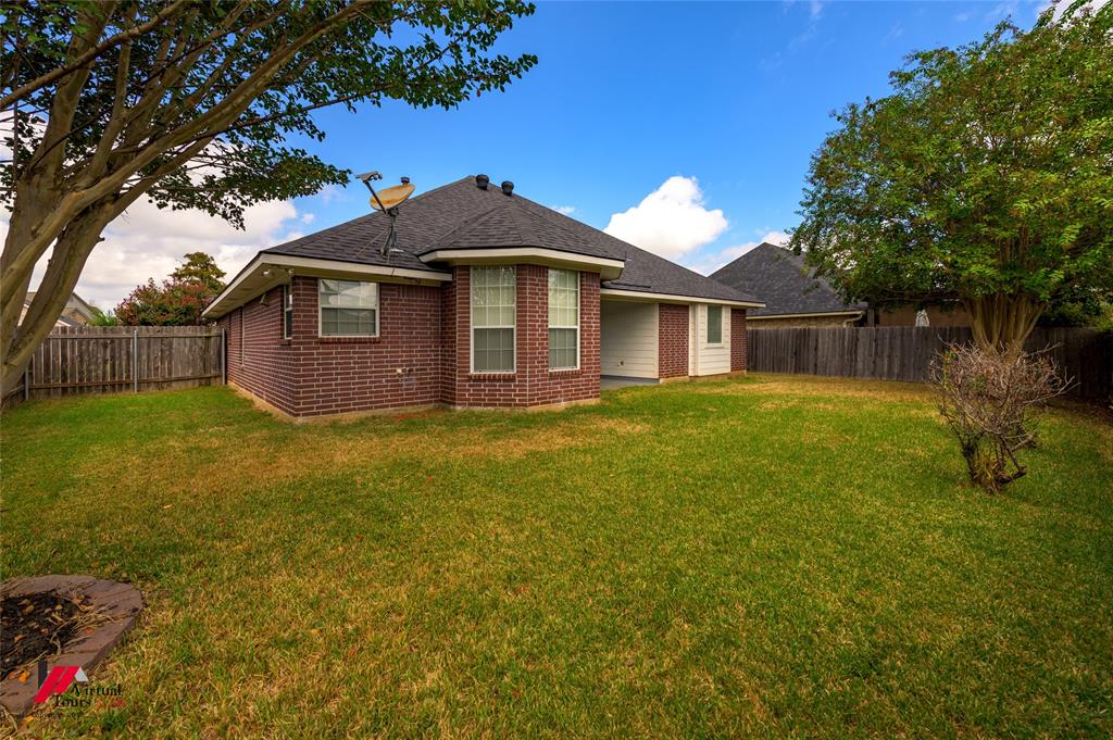 Rear elevation featuring a brick exterior, covered patio, hip roof, and fenced backyard with mature trees