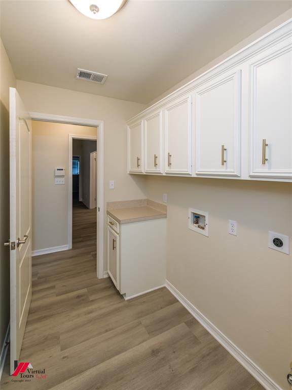 Laundry area featuring white shaker-style cabinetry with gold-toned hardware, solid surface countertop, and wood-finish flooring