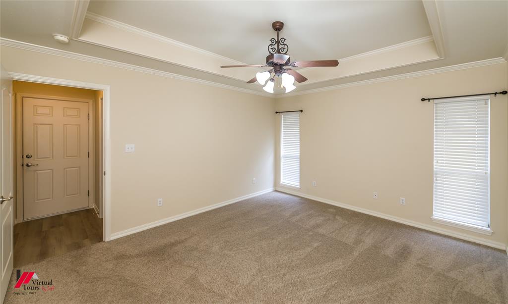 Tray ceiling featuring a decorative central ceiling fan with multi-light fixture, neutral carpeting, and dual windows with fitted blinds