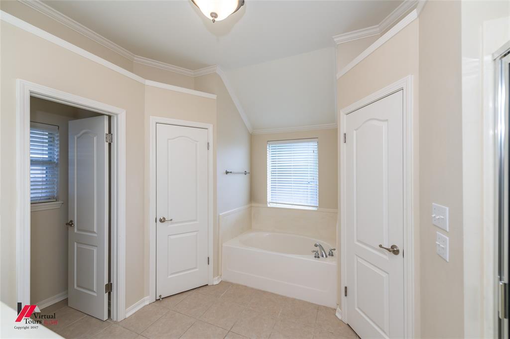 Bathroom featuring a vaulted ceiling, soaking tub with tile surround, neutral-tone ceramic tile flooring, and crisp white crown molding