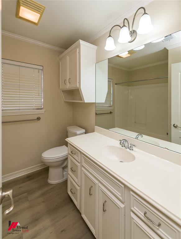 Bathroom featuring a vanity with white cabinetry, integrated sink, large wall-mounted mirror, overhead three-light fixture, and wood-finish flooring