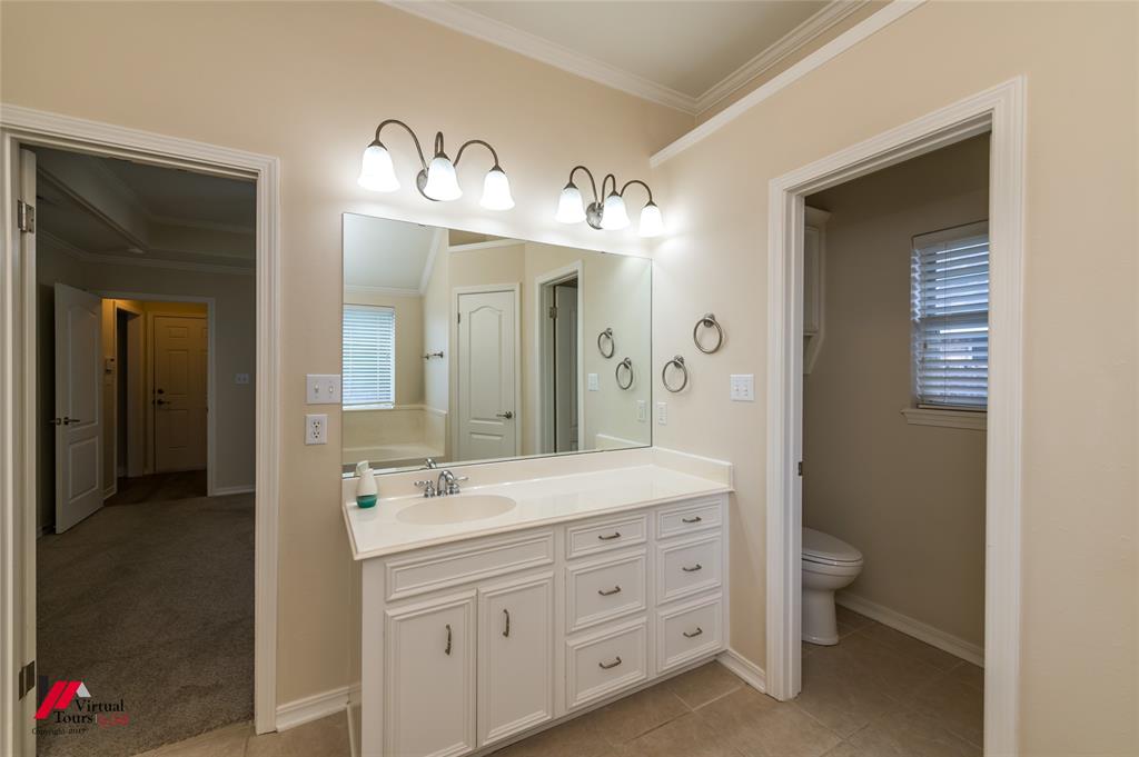 Bathroom featuring a white vanity cabinet with an integrated sink, a large frameless mirror, dual wall-mounted light fixtures, and ceramic tile flooring
