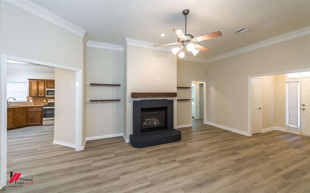 Living area featuring high ceilings with crown molding, wood-finish flooring, a central fireplace with a dark tile surround and wood mantel, and built-in wall shelving