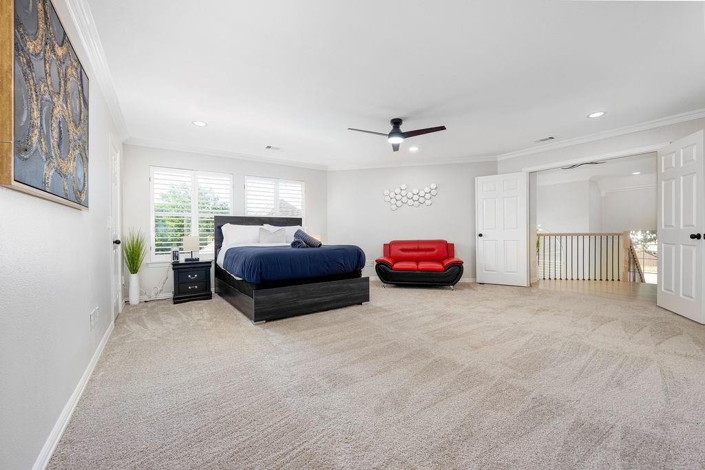Expansive room featuring light-toned carpeting, ceiling fan with integrated lighting, and multiple windows with plantation shutters