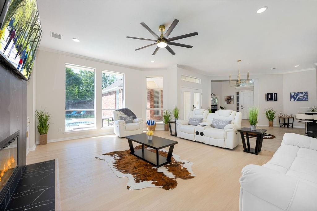 Recessed lighting, wood-finish flooring, a modern ceiling fan, a built-in fireplace with a black stone surround, and large windows