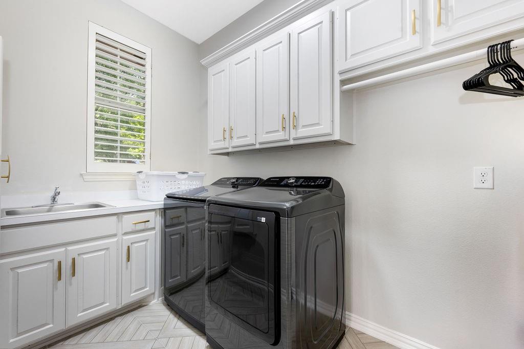 White cabinetry with gold-tone hardware, stainless steel sink, light-toned countertop, and herringbone-patterned flooring