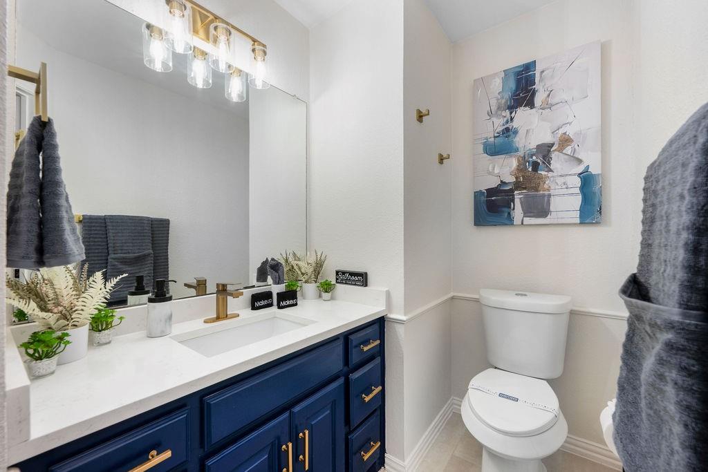 Single vanity with a white countertop and integrated sink, gold-finish faucet, and blue cabinetry with gold-finish hardware