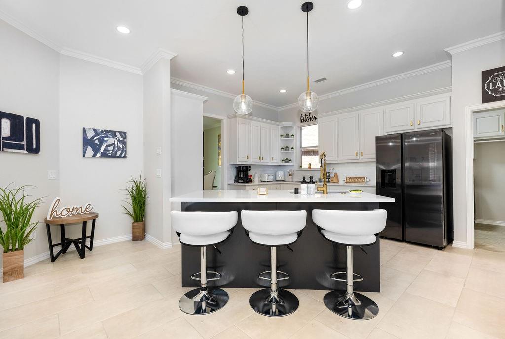 Kitchen featuring a central island with white countertop, white upper and lower cabinetry, black stainless steel refrigerator, and recessed lighting