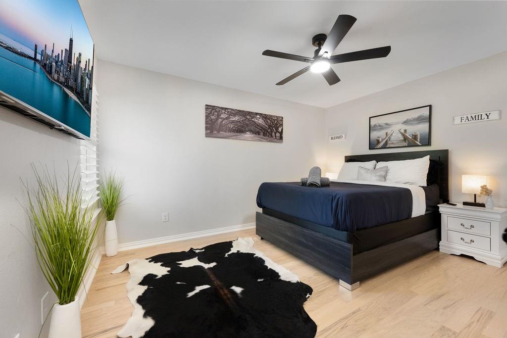 Light wood-finish flooring, a contemporary ceiling fan, and a built-in wall-mounted television