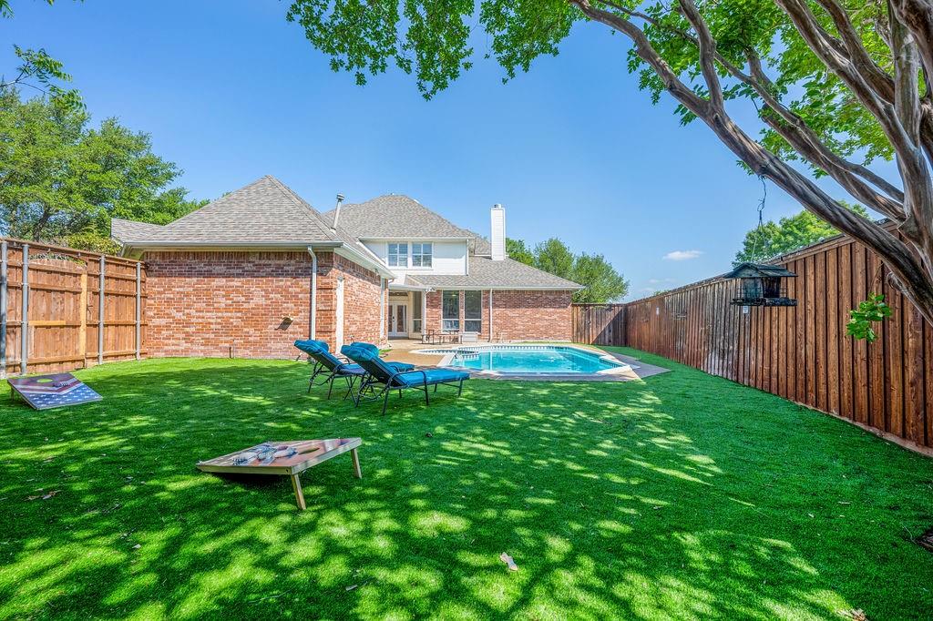 Spacious backyard featuring artificial turf, a rectangular swimming pool, and wood privacy fencing