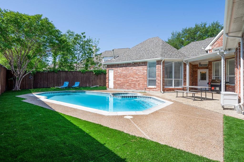 In-ground swimming pool with a textured concrete deck and surrounding artificial turf