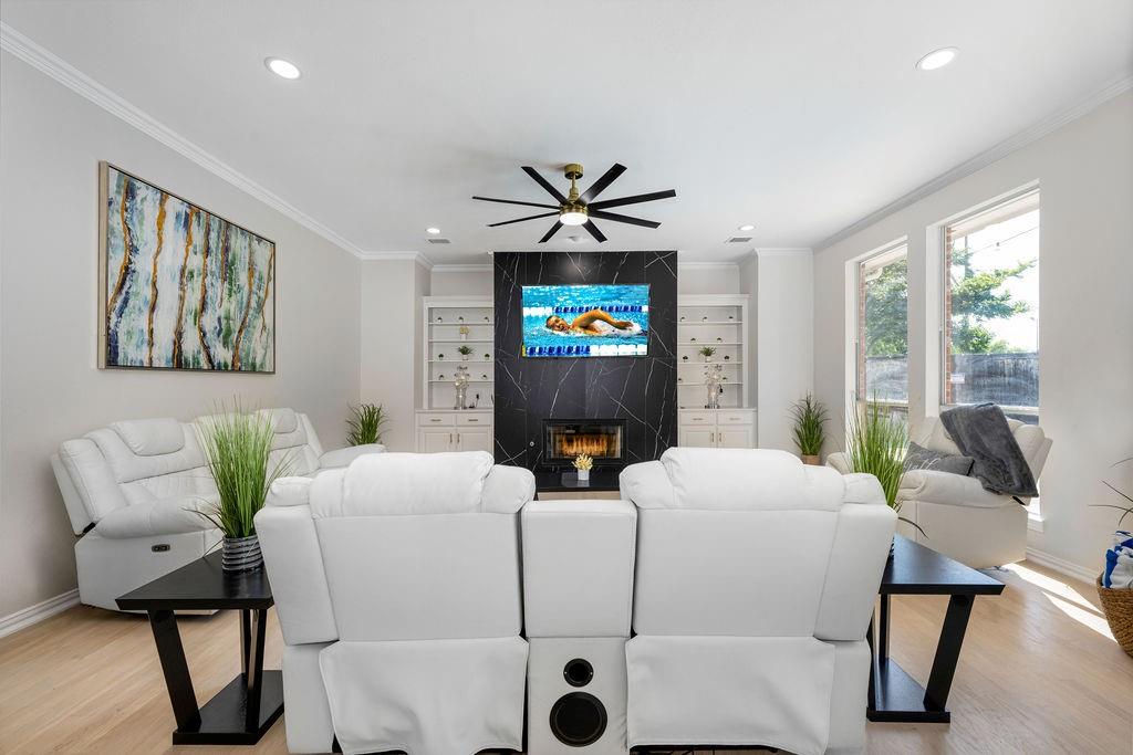 Recessed lighting, wood-finish flooring, crown molding, and a modern ceiling fan complement the black stone-clad fireplace with built-in shelving Recessed lighting, wood-finish flooring, crown molding, and a modern ceiling fan complement the black stone-clad fireplace with built-in shelving