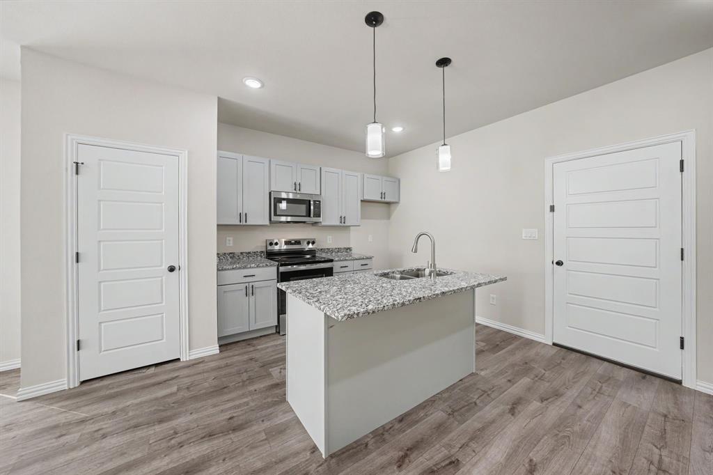 Kitchen featuring wood-finish flooring, light gray cabinetry, stainless steel appliances, a center island with a sink, and pendant lighting