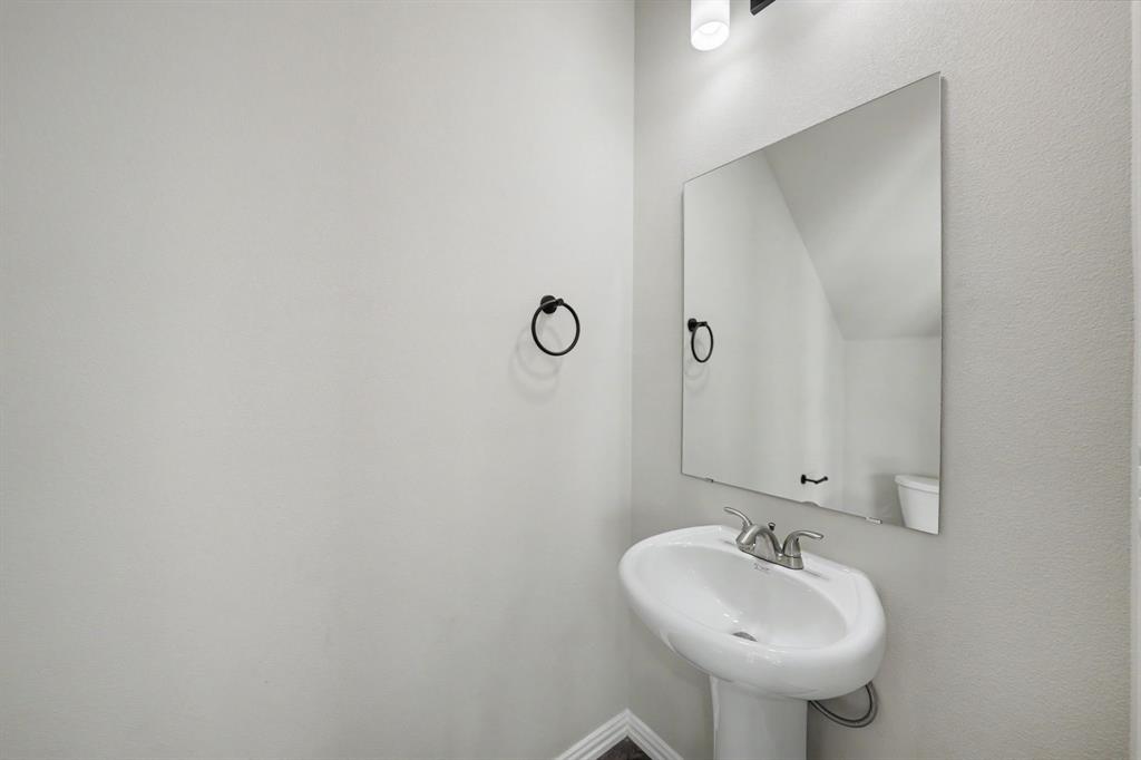 Pedestal sink with a chrome faucet, large wall-mounted mirror, and overhead vanity lighting
