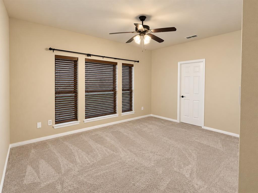 Neutral-toned walls, light-colored carpet, ceiling fan with integrated lighting, three windows with wood-finish blinds, and a paneled door