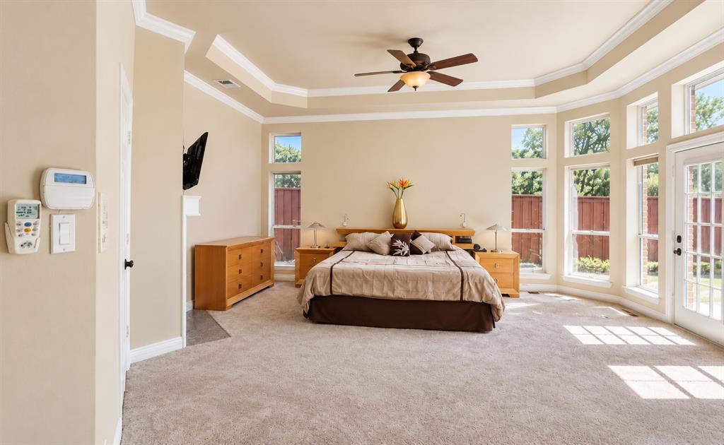Tray ceiling with crown molding, ceiling fan with integrated lighting, multiple tall windows, and a glass-paneled door