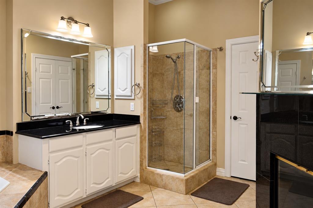 Tile flooring, white vanity with black countertop, glass-enclosed shower, wall-mounted vanity lights, and a large wall mirror