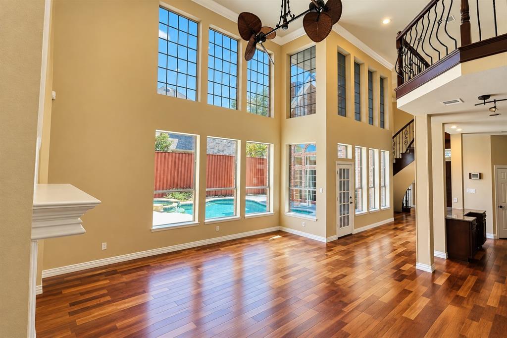 Two-story living area with high ceilings, featuring wood-finish flooring, an ornate staircase, and multiple windows providing ambient light and a pool setting