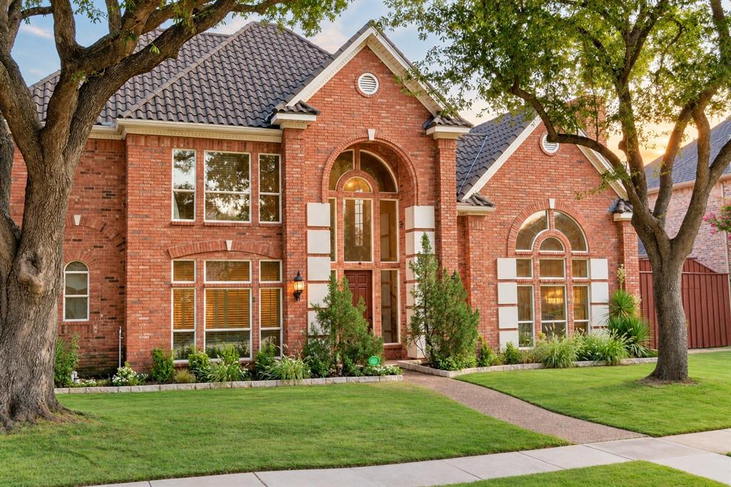 Brick exterior facade with a tiled roof, arched entry, expansive windows, and a paved walkway