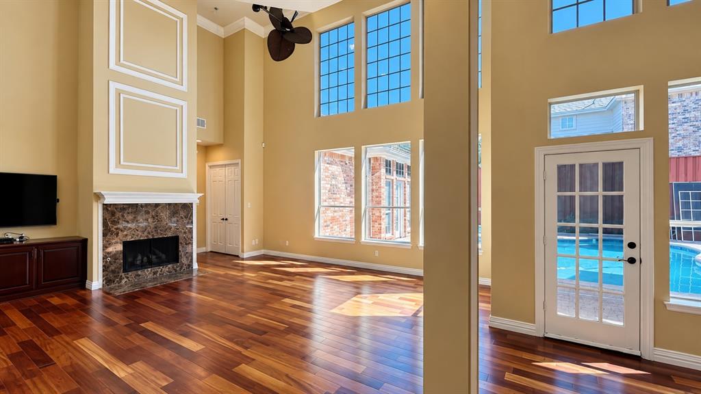 Hardwood flooring throughout, tall ceilings, multiple large windows, a fireplace with a stone surround, and a glass-paned door