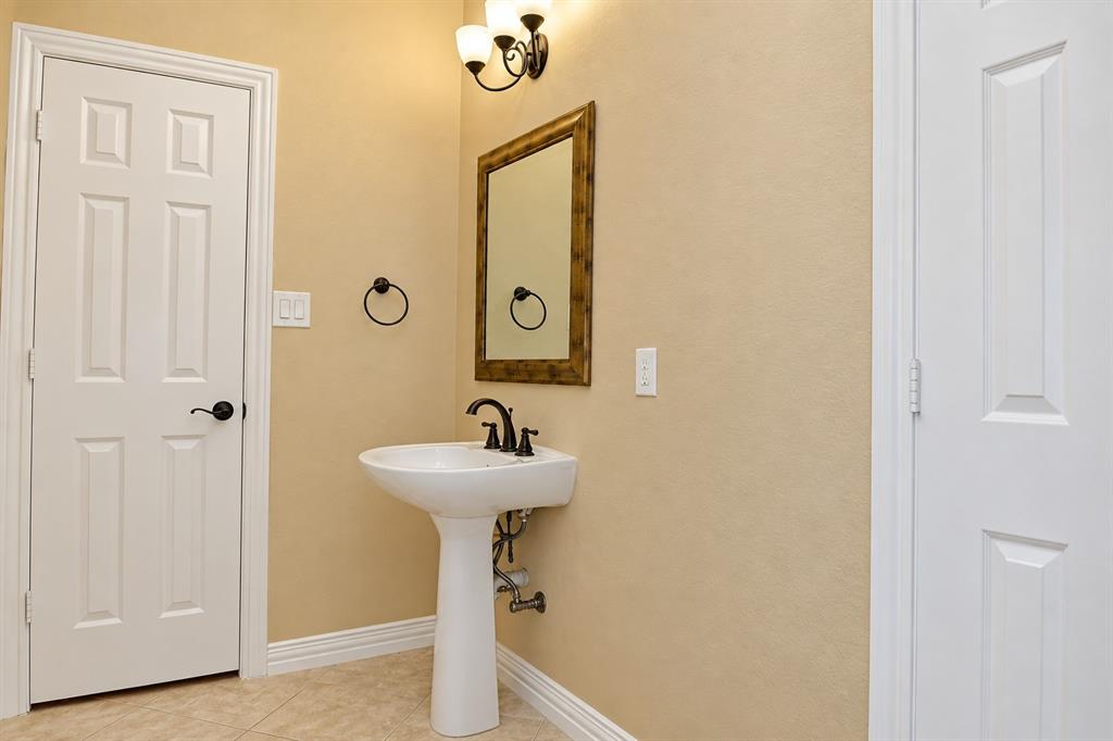 Pedestal sink with dark bronze faucet, framed mirror, and wall-mounted light fixture