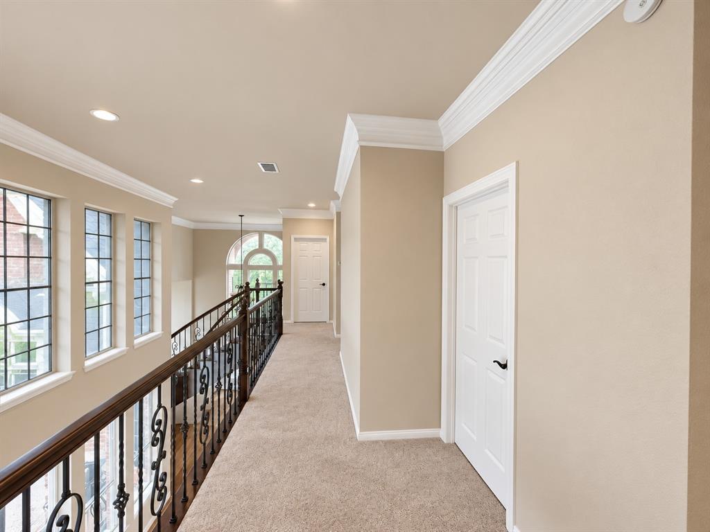 Upper-level hallway featuring a decorative wrought iron railing, arched window, recessed lighting, and crown molding