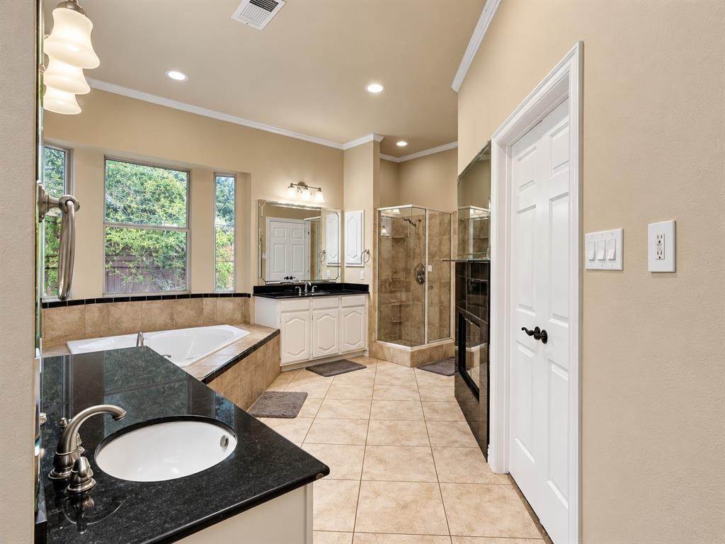 Dual vanities with undermount sinks and dark countertops, separate soaking tub, and a glass-enclosed shower