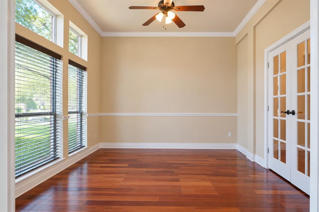 Rich wood-finish flooring, full-light French doors, crown molding, chair rail detailing, and a ceiling fan with integrated lighting