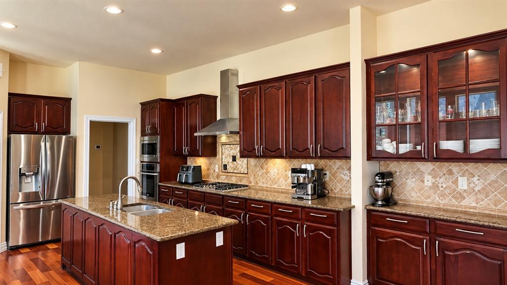 Kitchen featuring wood-finish flooring, an island with an integrated sink, granite countertops, and stainless steel appliances