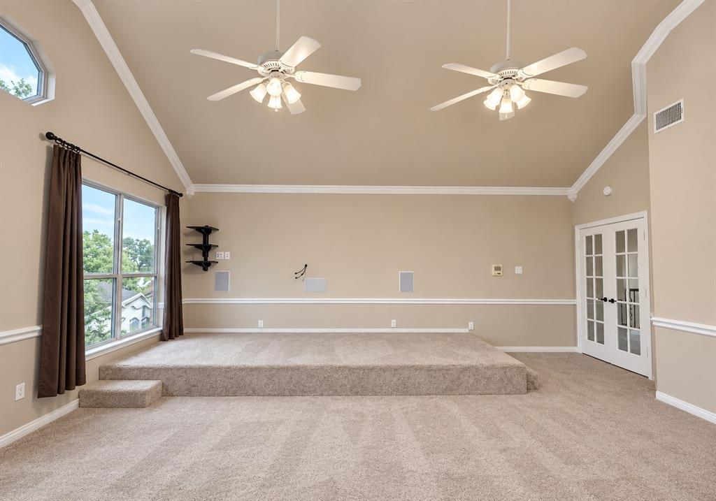 Vaulted ceiling with dual ceiling fans, elevated carpeted platform, large windows, and French doors