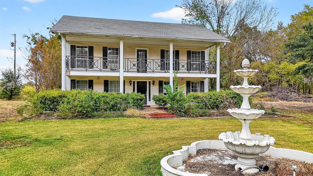 Two-story exterior with a full-width upper balcony, lower porch with columns, decorative iron railings, and a three-tiered fountain