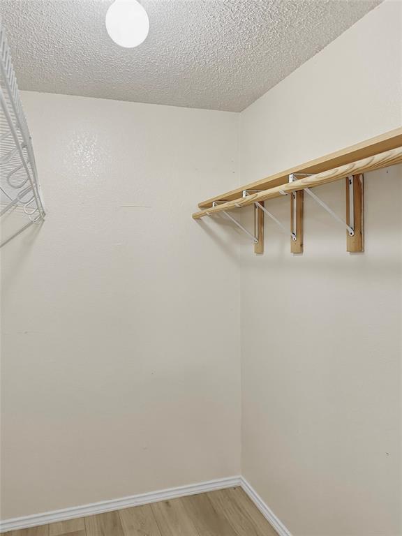 Spacious walk-in closet featuring natural wood-finish shelving and hanging rod system, recessed ceiling lighting, and wood-finish flooring throughout