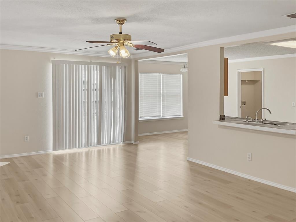 Wood-finish flooring throughout, sliding glass door with vertical blinds, ceiling fan with integrated lighting, breakfast bar with double basin sink, and crown molding accents