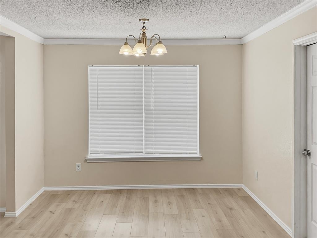 Wood-finish flooring, crown molding, white window blinds, and a brass-tone chandelier with frosted glass shades
