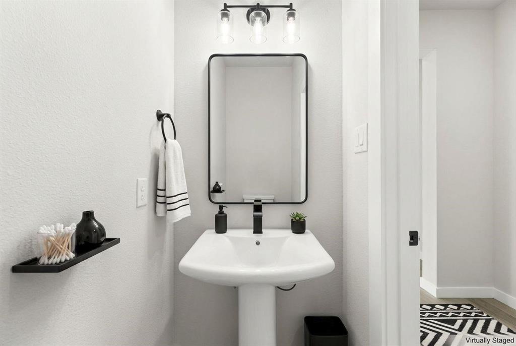 Pedestal sink with a single-handle matte black faucet, rectangular mirror with a matte black frame, and a three-light vanity fixture