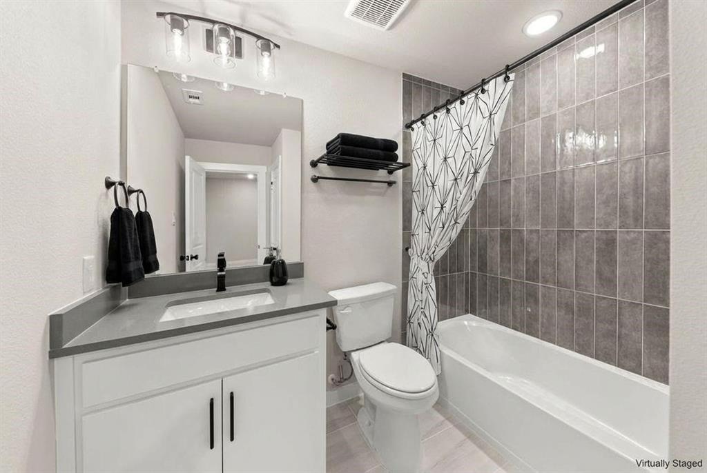Bathroom featuring a white vanity cabinet with a stone-composite countertop, undermount sink, matte black faucet, and vertical-set grey tile bathtub surround